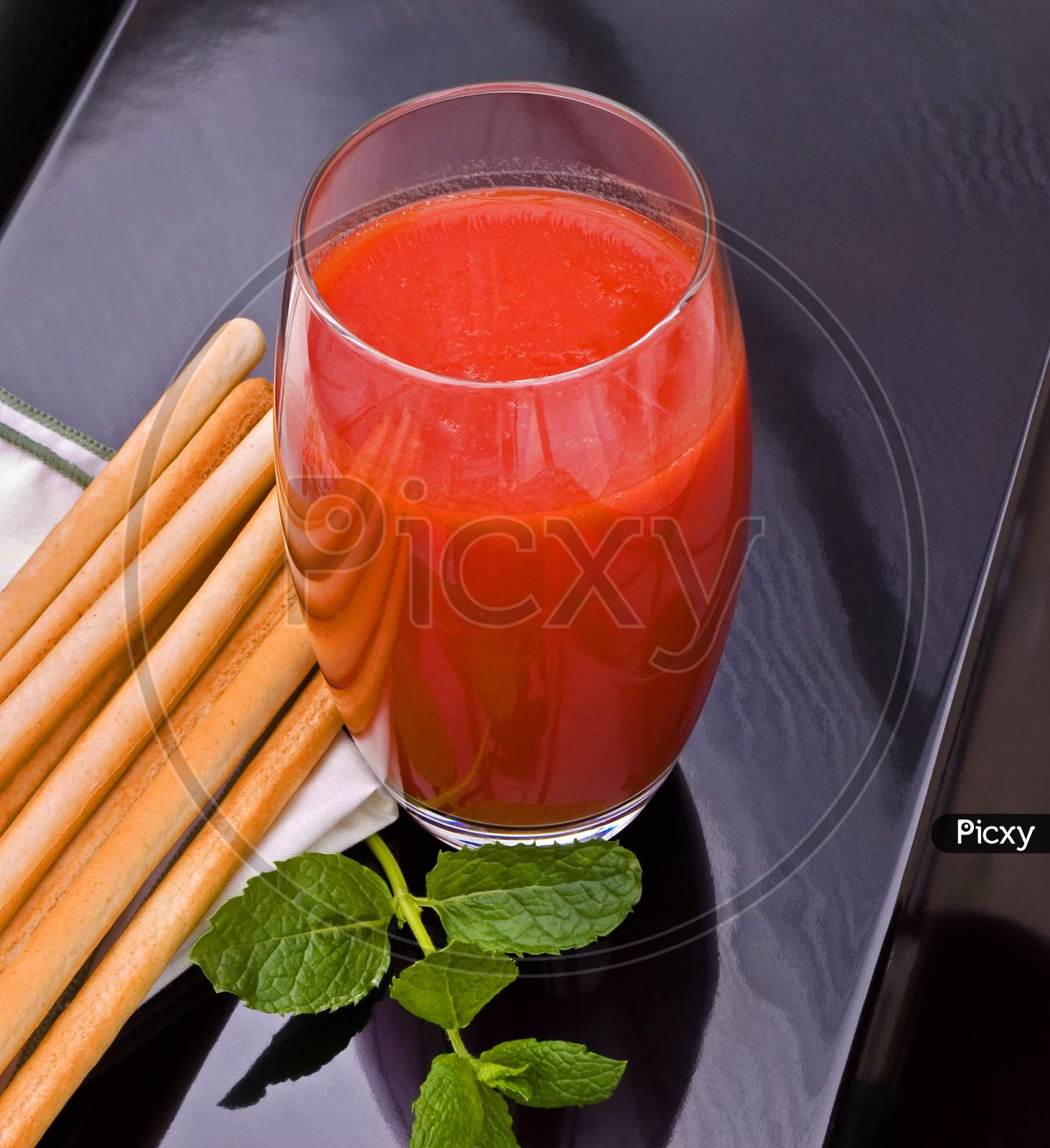 A glass of tomato juice with savoury bread sticks and mint.