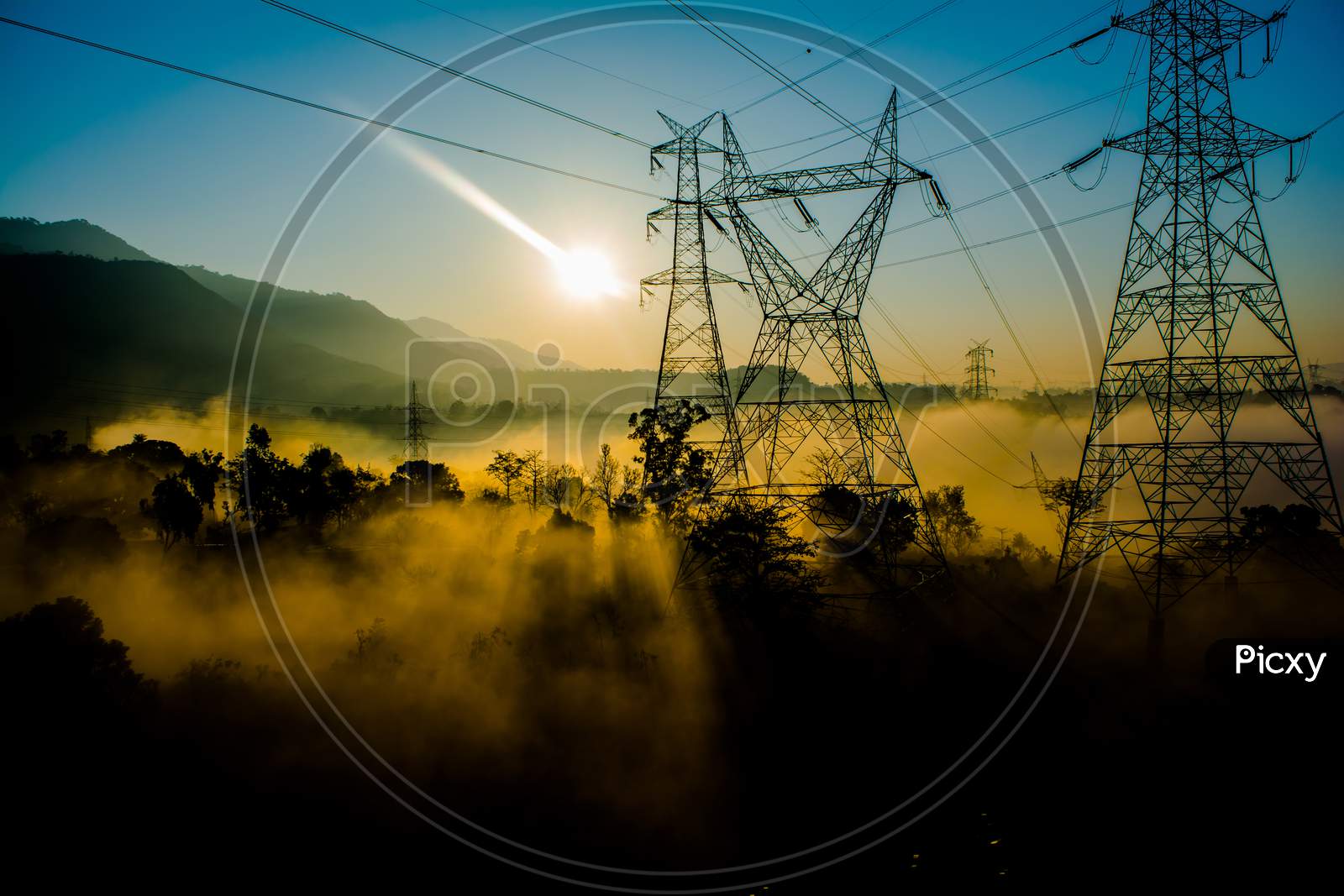sun rays coming through the trees and electric towers with fog enhancing the light at sunrise, Aerial view