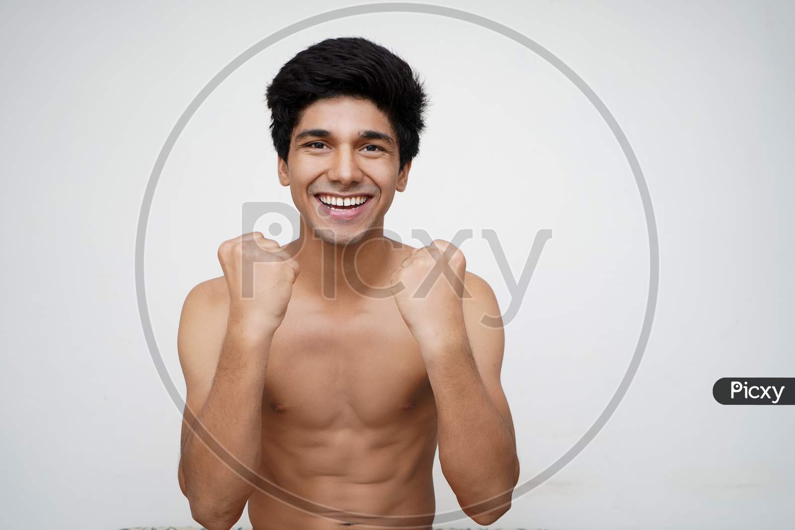 Hurray and cheers. Portrait of young handsome shirtless indian model looking excited while standing against white background