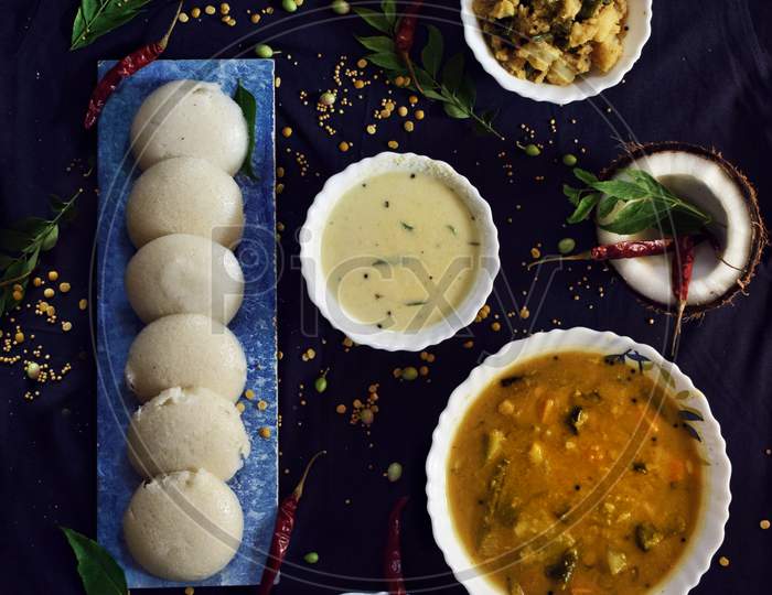 A South Indian thali composed of dhosa,idlies,uttapam,sambar and coconut chutny on a black background.