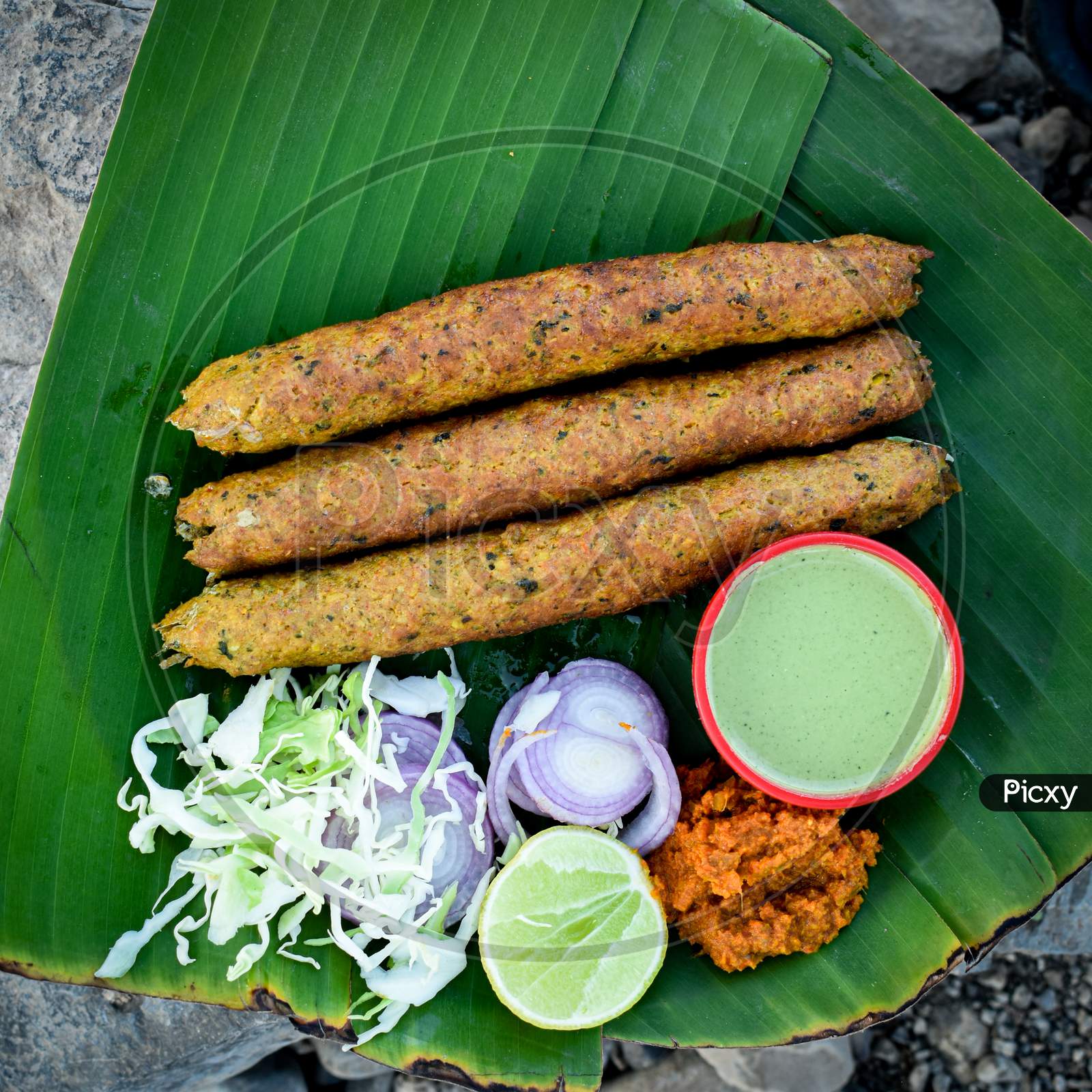 Seekh kebab on and chicken pieces on banana leaf, top view