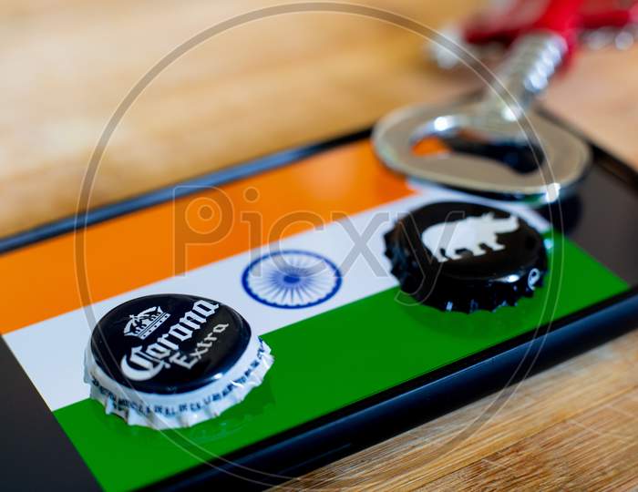 Mobile Phone With India Flag And Two Beer Bottle Caps And An Opener On Wooden Board
