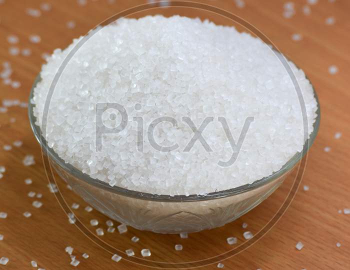 Sugar in glass bowl on wooden background