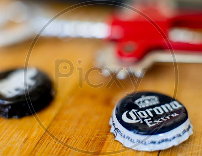 Shot Of Wooden Board With Mobile Phone, Bottle Opener, And Beer Bottle Caps Of Corona And White Rhino