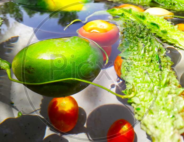 Green vegetables like raw mango and bitter gourd floating and drowned in water in sunlight  and shadows are formed on vessel