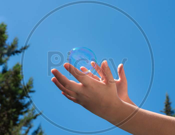 A Bubble Soap In Children Hands Against A Blue Sky