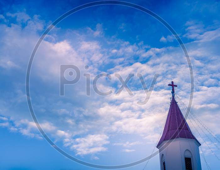 Church Roof With Cross Under Blue Moody Cloudy Sky And Some Copy Or Text Space.