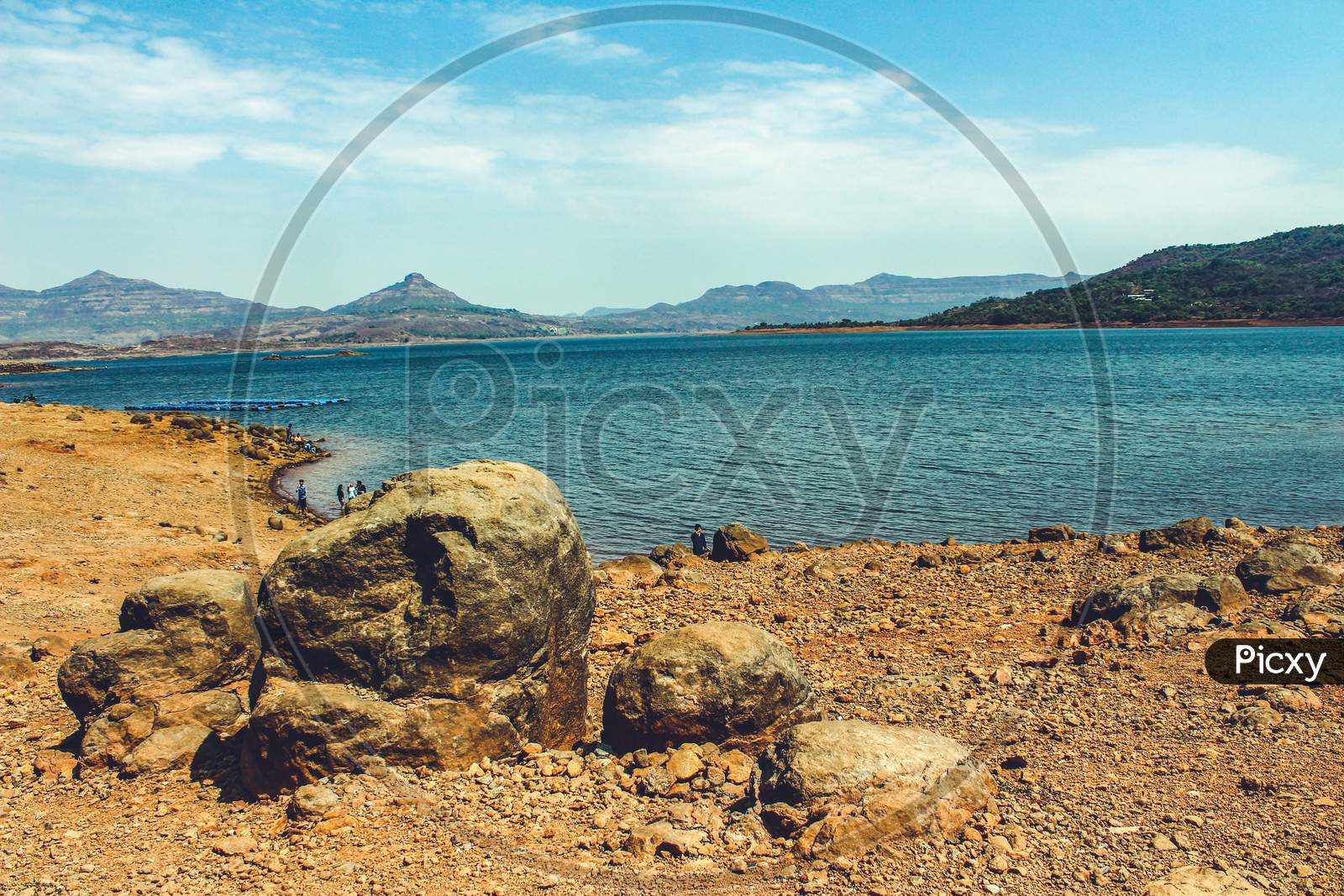 Landscape Of A Lake From Its Rocky Shore With Mountains In The Background