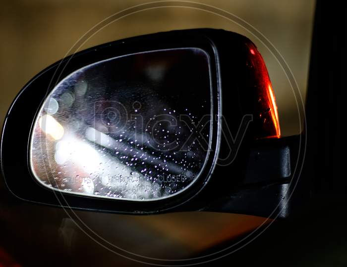 Car Side-Mirror With Raindrops And Reflection At Night While Driving