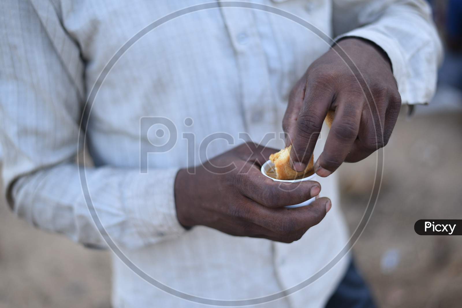 A migrant worker dips a biscuit in tea