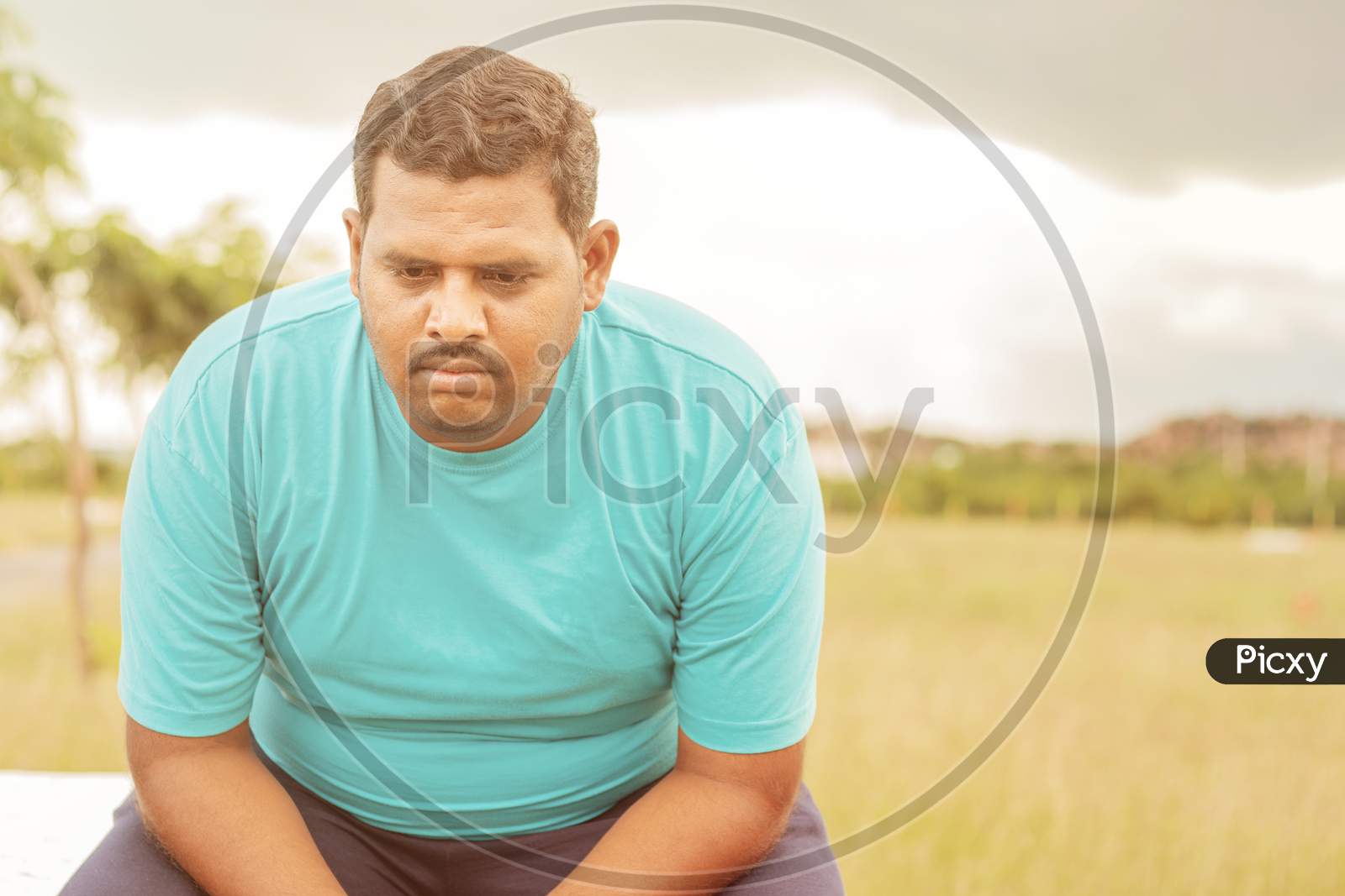 Seriously Fat Man On Outdoor, Park - Concept Of Sadness Due Overweight - Indian Obese Man Feeling Unhappy Or Depressed.