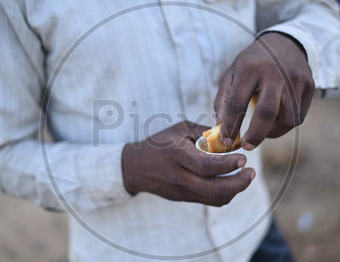 A migrant worker dips a biscuit in tea