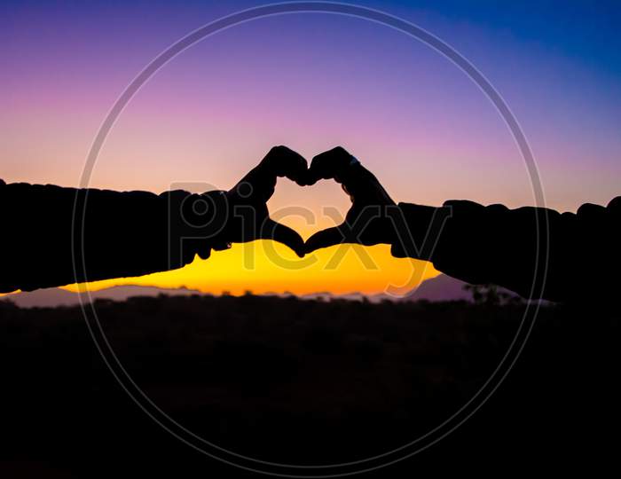 heart shape by hands in silhouette while watching the sunset