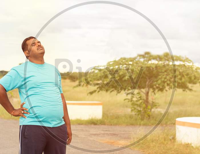 Tired Young Obese Man Holiding His Back While Jogging - Concept Of Fat Man Fitness And Unhealthy Lifestyle.