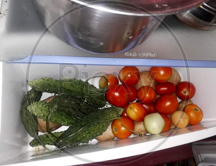 fresh tomatoes, potatoes and bitter gourd in the vegetable section or vessel of a refrigerator