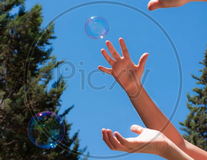 Soap Bubbles In Children Hands Against A Blue Sky
