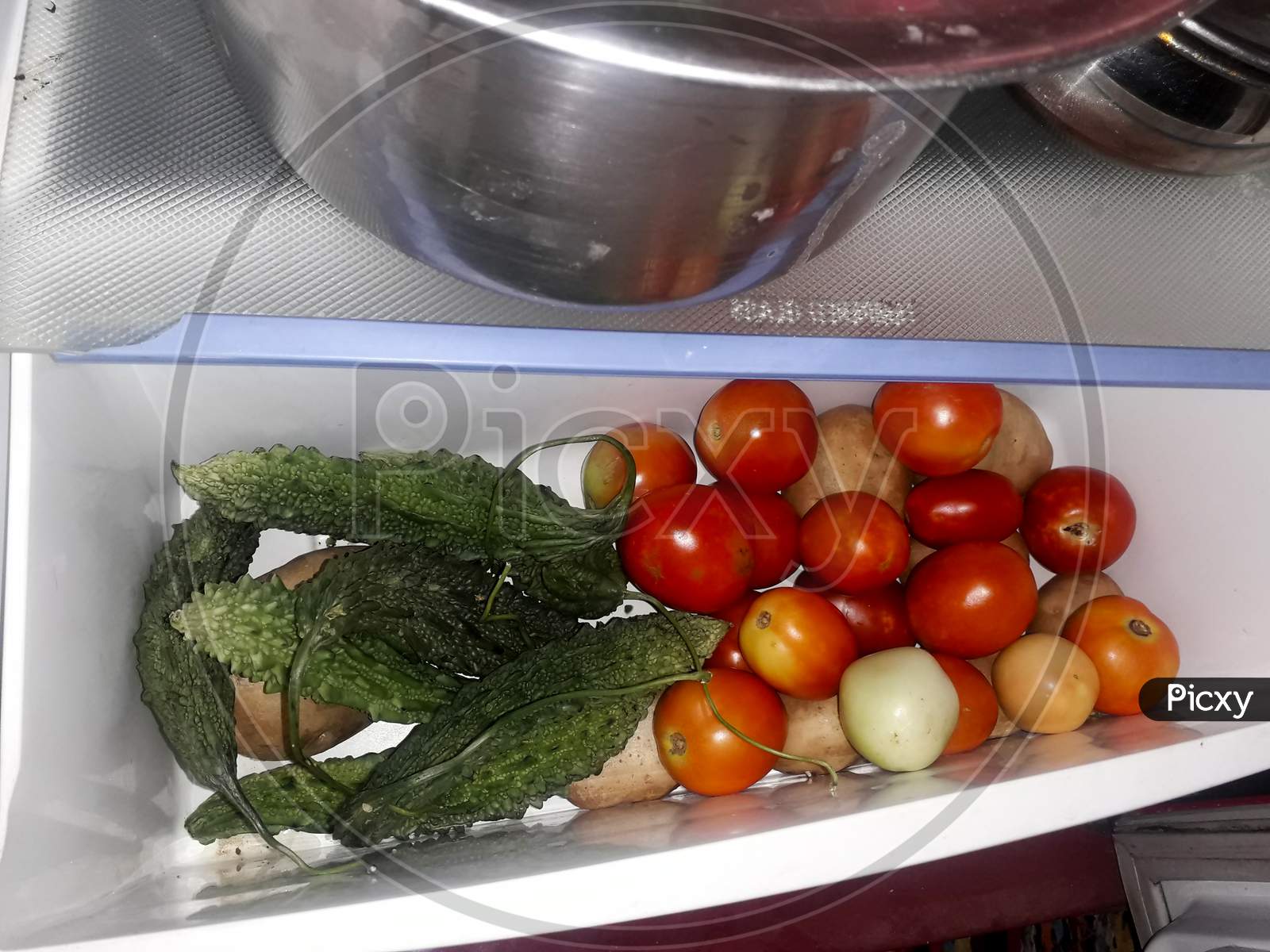 fresh tomatoes, potatoes and bitter gourd in the vegetable section or vessel of a refrigerator