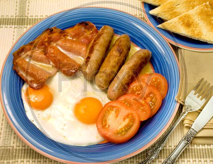 Typical English breakfast with egg sausage bacon and tomatoes.