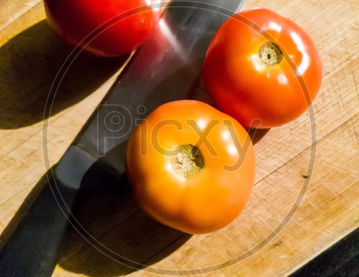 Fresh tomato ready to be cut with a knife on a chopping board with natural light.