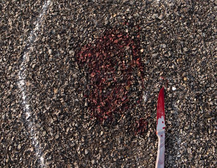Close Up Of Crime Scene Chalk Outline Of Victim Dead Body On Road With Bloody Knife And Blood.