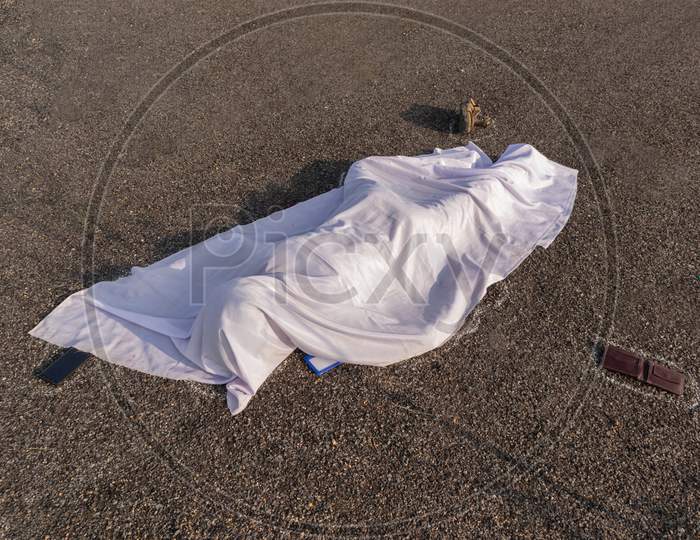 Concept Of Road Accident Scene, High Angle View Of Chalk Outlined Dead Body Covered Under White Cloth Laying On Road.