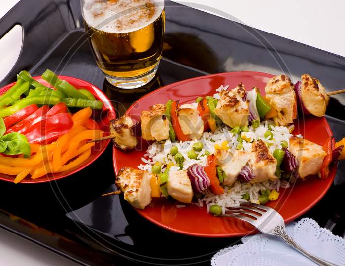 Two kebab sticks with rice and beer on a tray