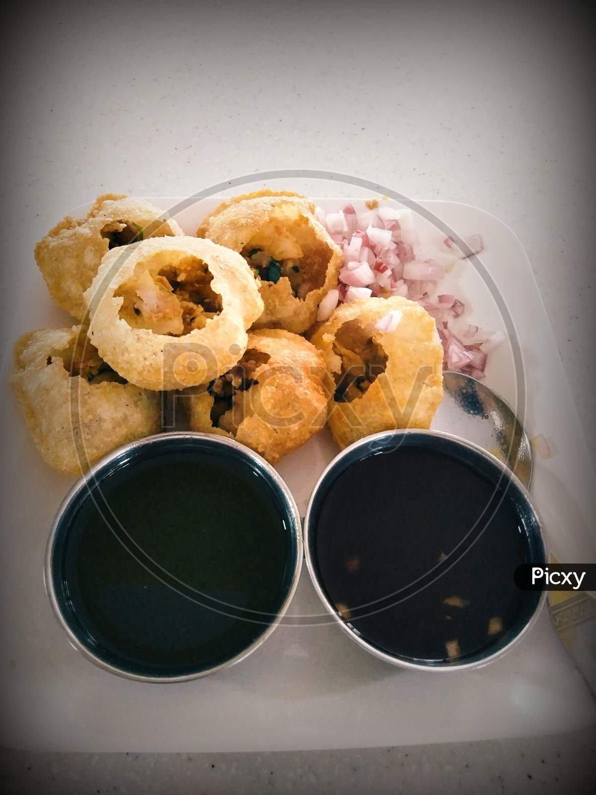 Sweet And Spicey Panipuri With Different Chutney And Onions And Stuffing On White Plate With Spoon