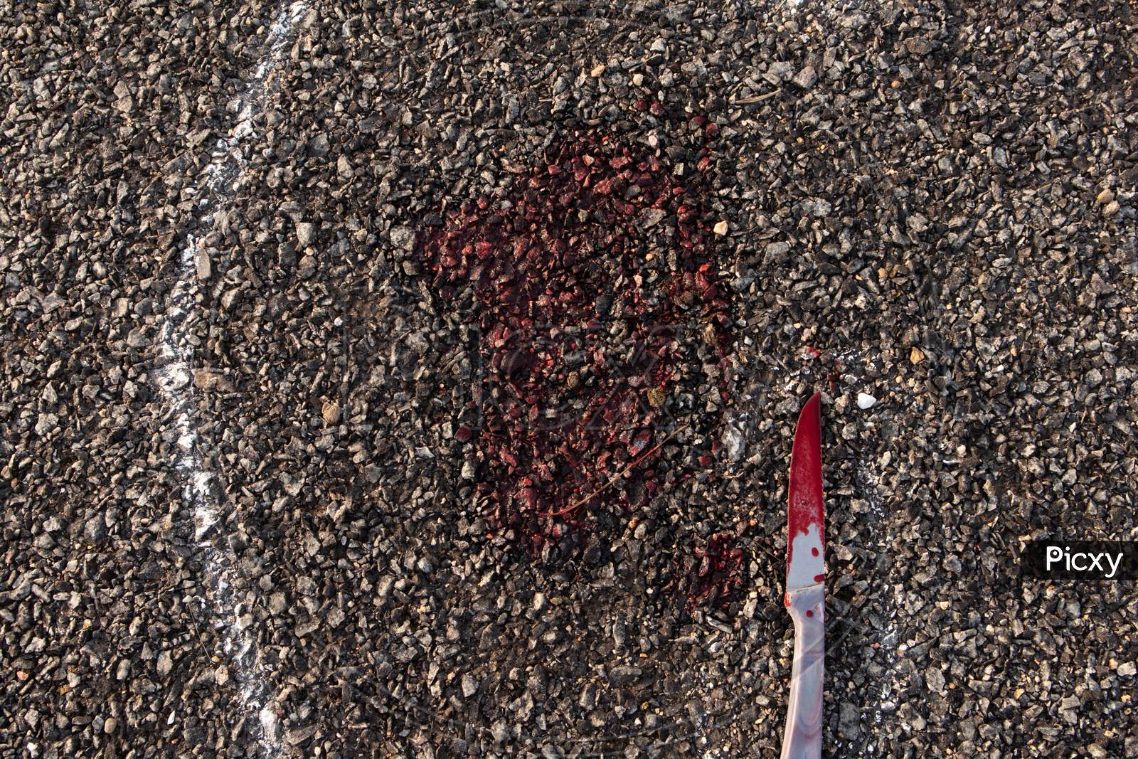 Close Up Of Crime Scene Chalk Outline Of Victim Dead Body On Road With Bloody Knife And Blood.