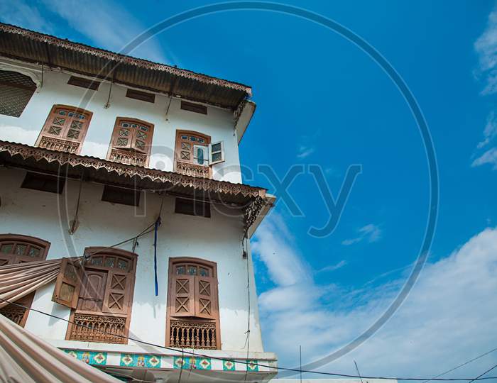 Traditional House Architecture Of A White Building With Many Wooden Doors And Windows Against Blue Sky, Element Of Architectural Decoration Of The Facade Of The Building