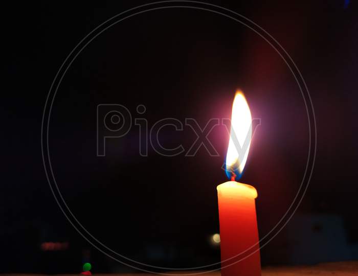 A CANDLE FLAME GIVE LIGHT IN DARK NIGHT WITH LIGHT BILINKING BEHIND