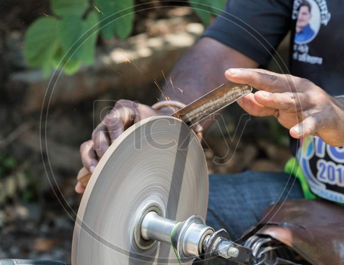 An Indian Man Sharpening A Knife On Rotating Whetstone