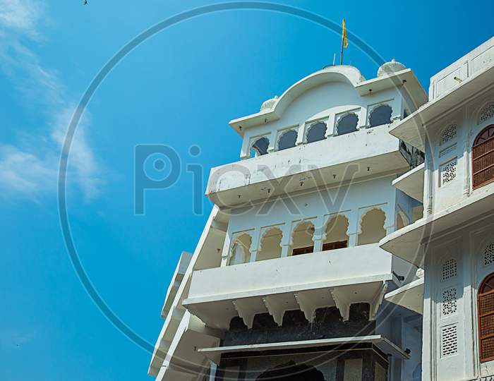 Traditional House Architecture Of A White Building With Many Wooden Doors And Windows Against Blue Sky, Element Of Architectural Decoration Of The Facade Of The Building