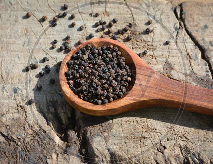 Black peppercorns in wooden spoon on wooden background