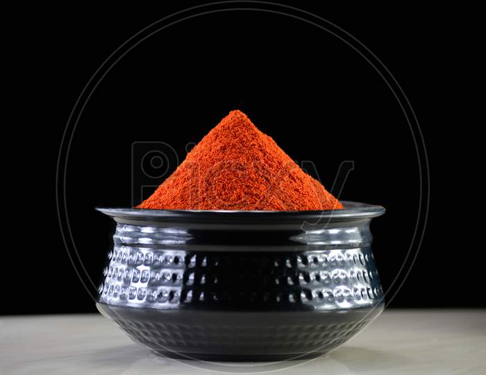 Red chili powder in black bowl on dark background