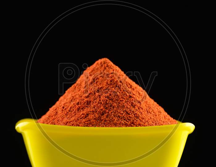 Red chili powder in yellow bowl on dark background