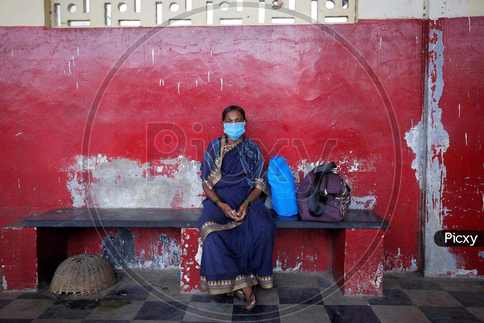 A woman wears a mask and waits for a public transport bus in a bus station after the state eased lockdown norms during the nationwide lockdown to prevent the spread of coronavirus (COVID-19) in Bangalore, India.