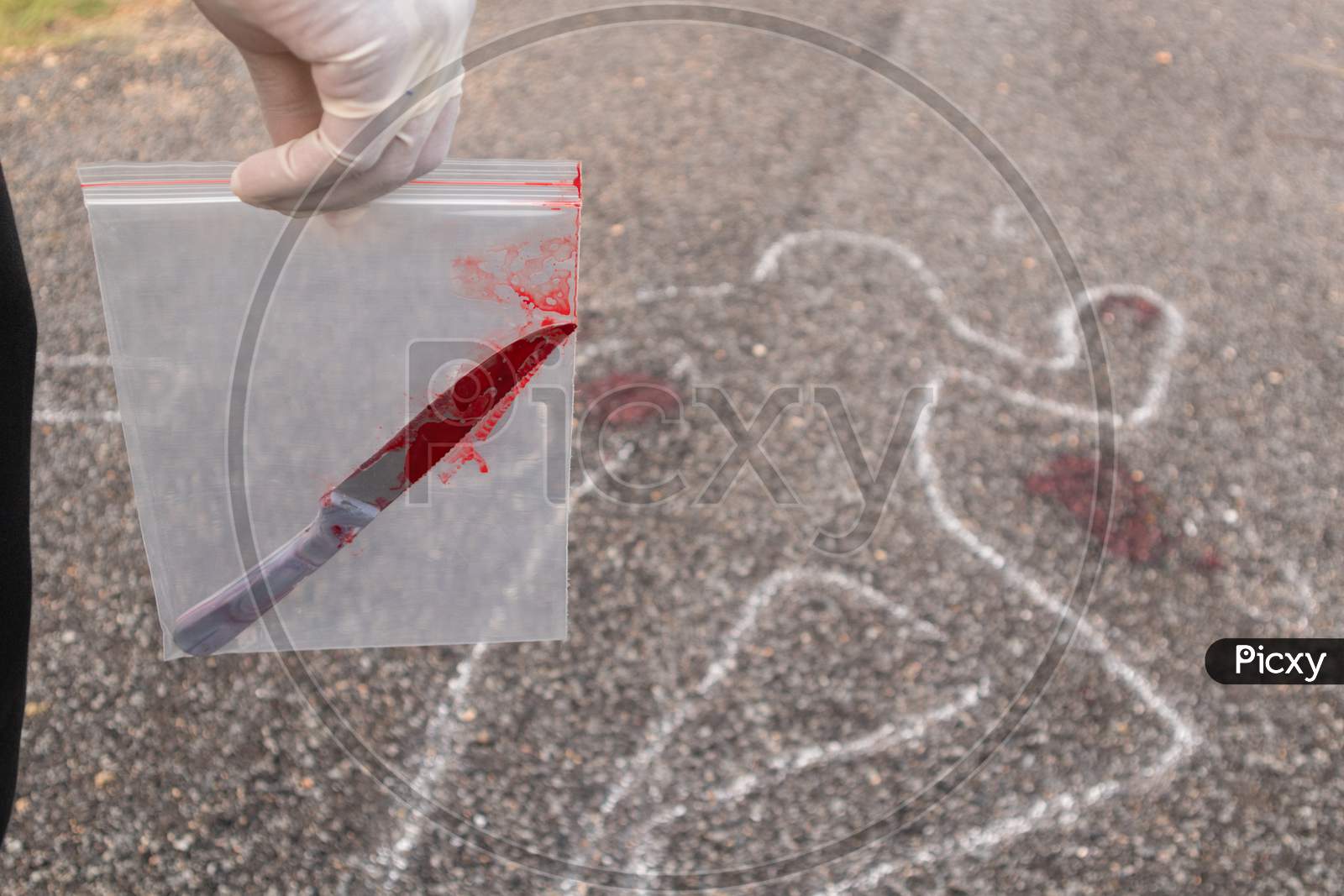 Concept Of Crime Scene Investigation, Detective Or Investigator Holding Evidence Bag With Bloody Knife In Bag And Chalk Outlined Dead Body As A Background