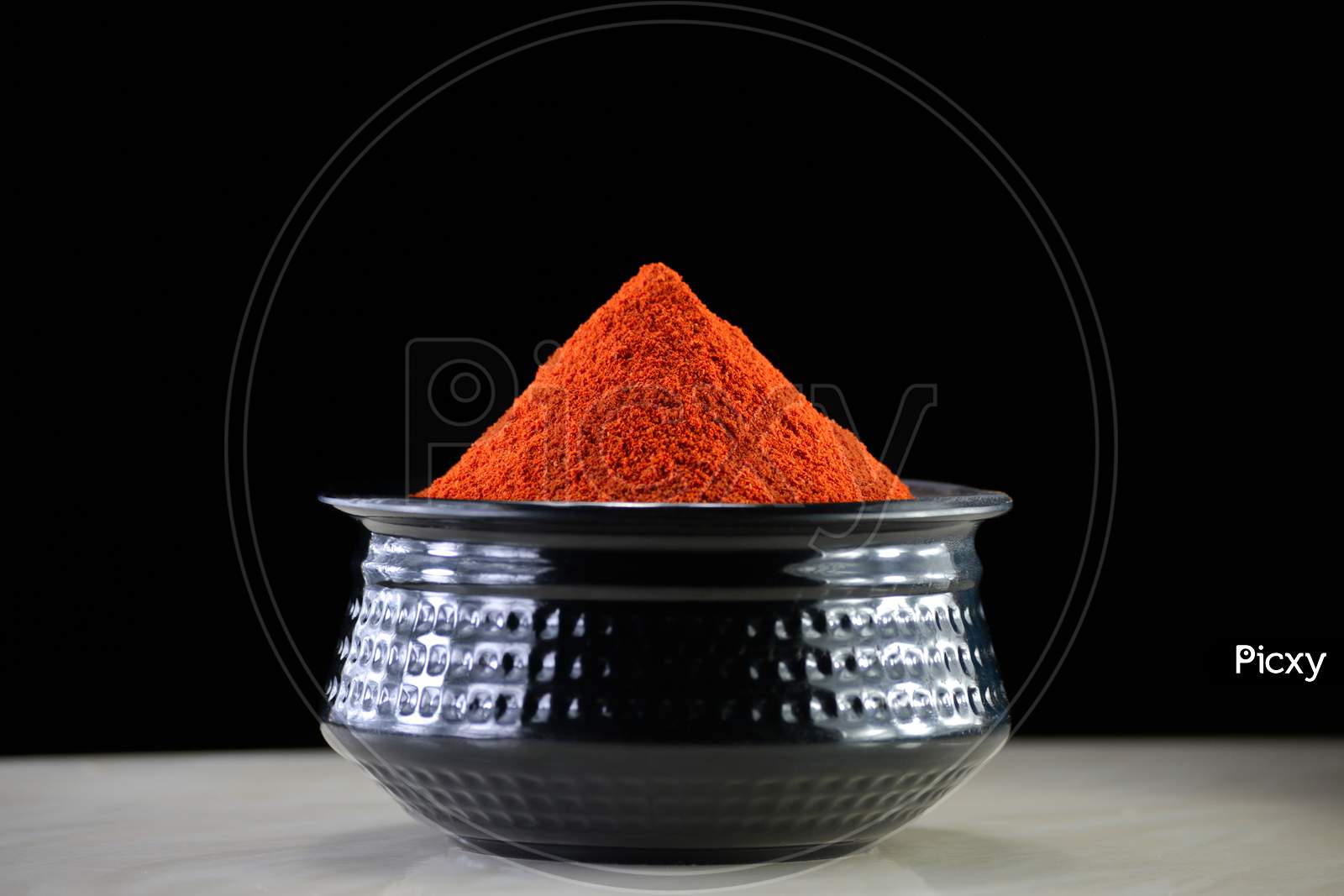 Red chili powder in black bowl on dark background