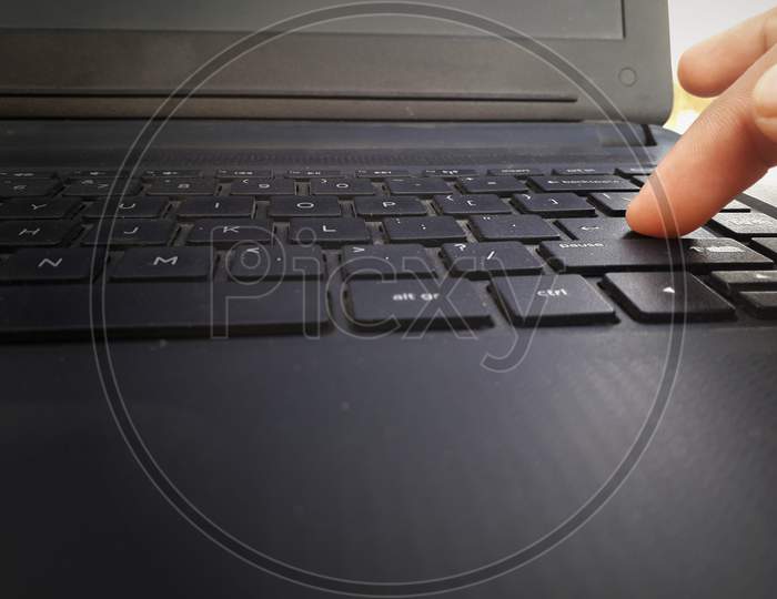 An Asian male is pressing the enter key in keyboard in a black colored laptop -closeup view
