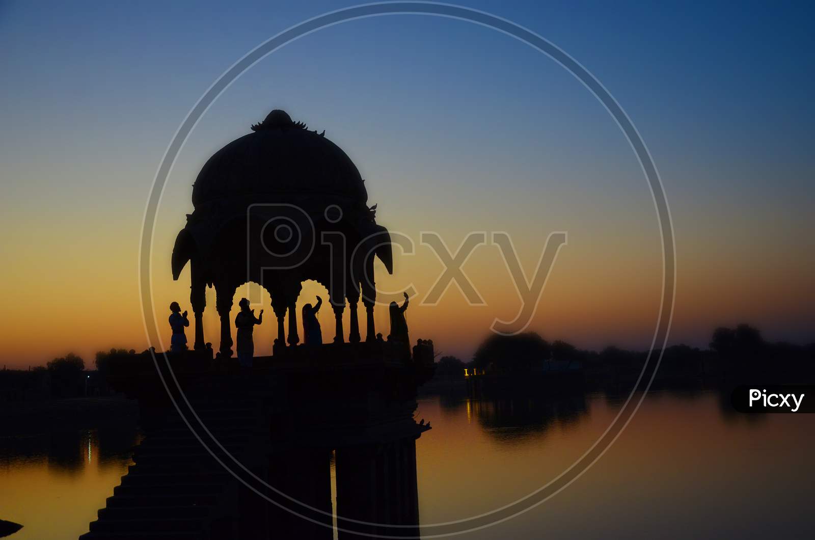Silhouette Of Temple On The Gadi Sagar Lake With Four People Standing Sunset Sky In Jaisalmer, Rajasthan, India