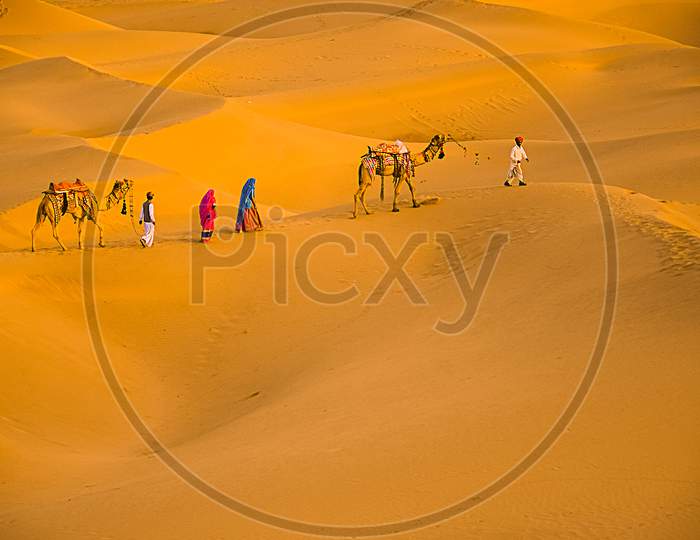 Jaisalmer, Rajasthan, India - April 18Th, 2018: Cameleers With Camels Walking On Golden Sand Dunes Of Thar Desert, Jaisalmer, Rajasthan, India