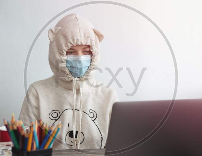 Young woman girl wearing mask and funny hoodie looking bored in front of laptop at home. Work from home during covid quarantine concept