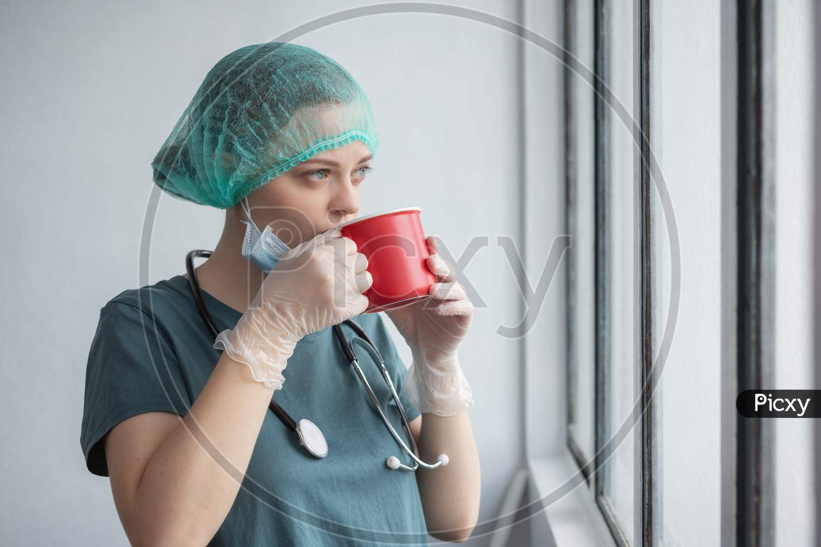 Young caucasian female doctor nurse in surgical mask looks tired. Coffee break during coronavirus covid-19 outbreak
