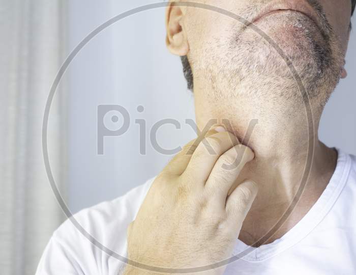 White-Skinned Man With A Half-Grown Beard Wearing A White T-Shirt On A Neutral Background While Scratching His Neck. Free Space To Write.