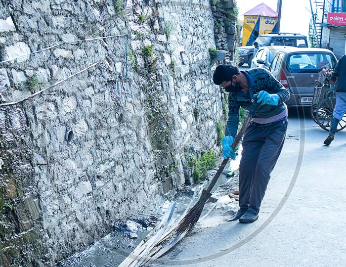 Shimla, Himachal Pradesh, India - July 20Th, 2019: Municipal Worker Sweep The Road And Drainage With Broomstick And Collects Garbage, Sanitation Worker Sweep Street