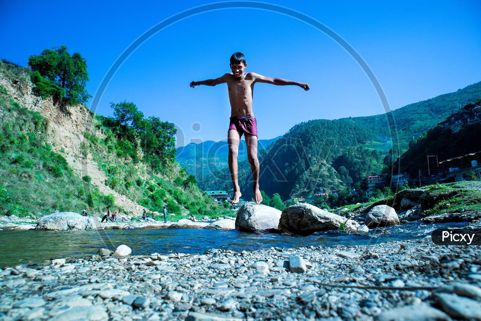 Nerwa, Himachal Pradesh, India - July 20Th, 2019: Young Boy Jumping Into The River Water With Beautiful Mountains Hills Covered With Trees In The Background,