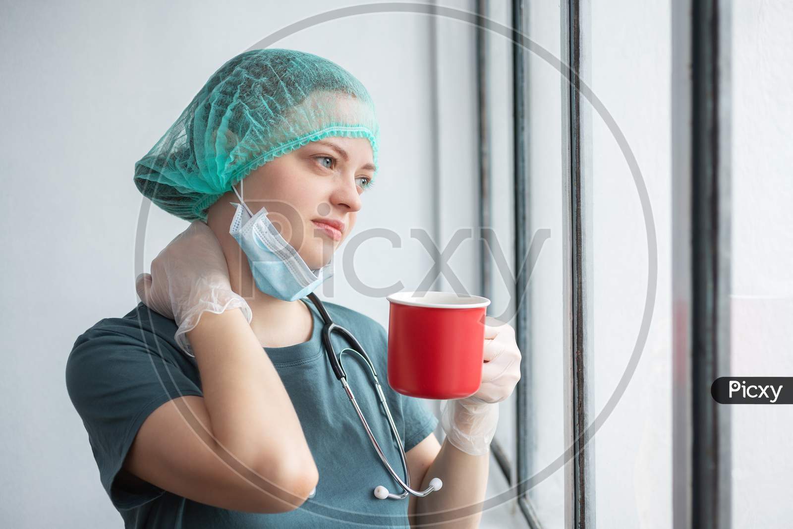 Young caucasian female doctor nurse in surgical mask looks tired. Coffee break during coronavirus covid-19 outbreak