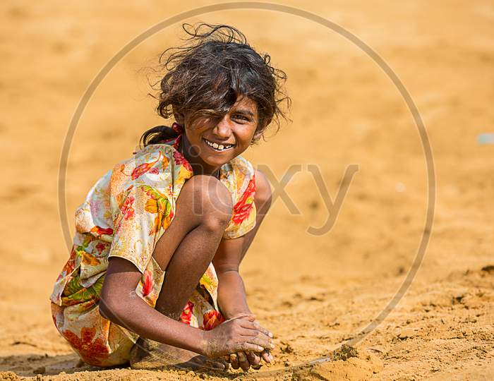 Jodhpur, Rajasthan, India - June 18Th, 2019: Poor Rural Girl Playing With Sand In Hot Summer, Smiling Towards Camera, Poverty Unprivileged Indian Children.