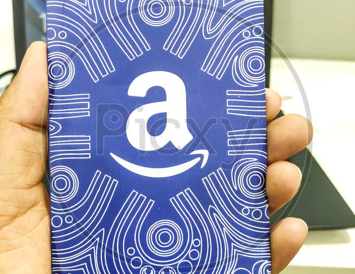 A hand holds a Amazon gift card, which allows the recipient to purchase items from the Amazon.com website