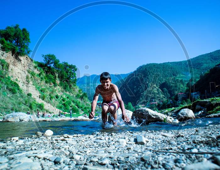 Nerwa, Himachal Pradesh, India - July 20Th, 2019: Young Boy Jumping Into The River Water With Beautiful Mountains Hills Covered With Trees In The Background,